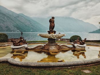 Statue by lake against sky