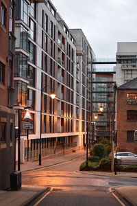 City street by buildings against sky at dusk