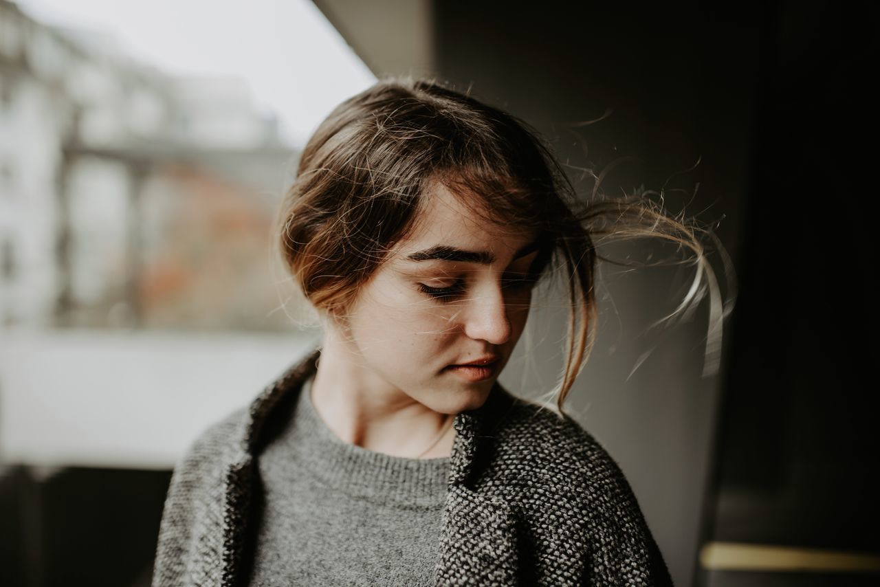 one person, headshot, real people, portrait, lifestyles, focus on foreground, front view, young adult, indoors, looking, casual clothing, looking down, close-up, young women, hairstyle, leisure activity, contemplation, home interior, warm clothing, beautiful woman, teenager, depression - sadness