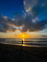 Silhouette woman walking at beach against sky during sunset