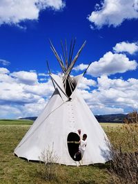 Boy standing by tent on landscape against sky