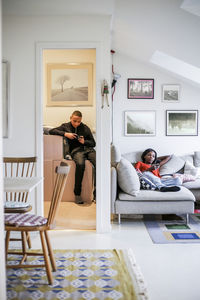 Mother using mobile phone on sofa while boy sitting in storage room at home