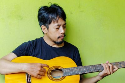 Young man playing guitar against wall