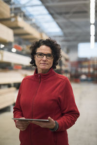 Portrait of confident female customer holding digital tablet while standing in hardware store warehouse