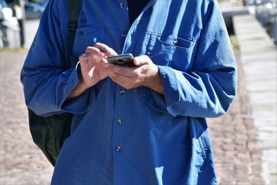 Midsection of mature man using mobile phone while standing on footpath