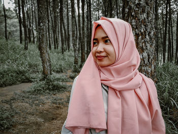 Portrait of woman standing by tree trunk in forest