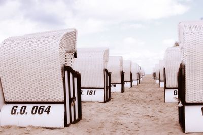 Hooded chairs on sand at beach against sky