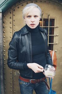 Portrait of woman holding container while standing against closed door