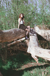 Full length of woman sitting on tree trunk in forest