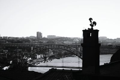 Silhouette bridge by cityscape against clear sky