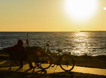 Man sitting by sea against clear sky during sunset