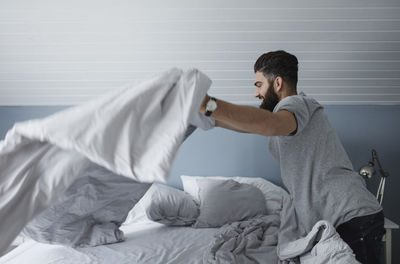 Side view of man making bed at home