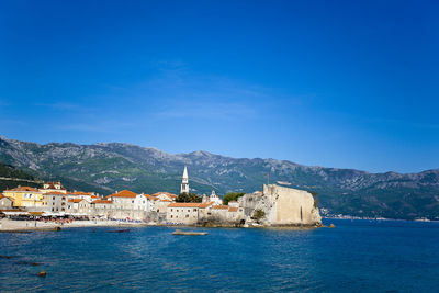 Buildings by sea against blue sky