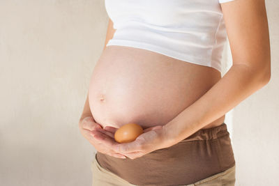 Midsection of pregnant woman holding egg against white background