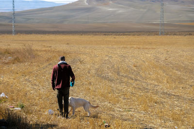 Rear view of man with dog walking on field