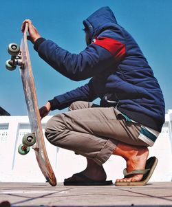 Low section of man sitting on metal against sky