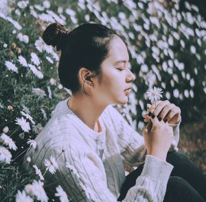 Side view of a young woman holding red flowering plants