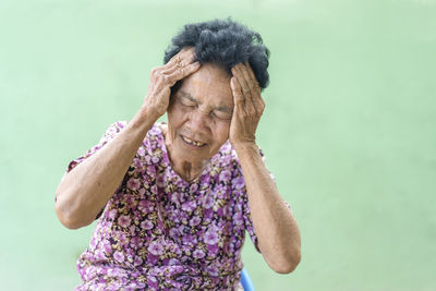 Senior black-haired woman touching head with hand with painful expression because of headache.