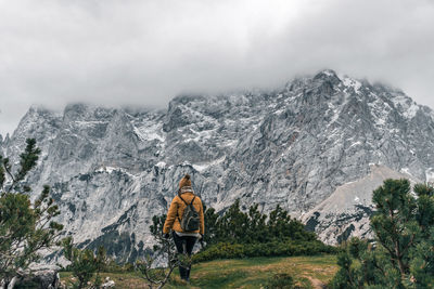 Back view of female hiker wearing winter clothes, standing on scenic viewpoint in amazing mountains