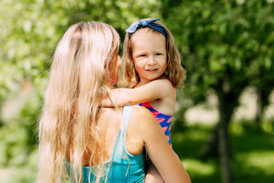 A young mother holds her little daughter in her arms on a summer day in the garden or park