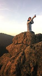 Man taking selfie on peak against sky during sunset