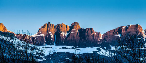 Low angle view of snowcapped mountains against clear blue sky