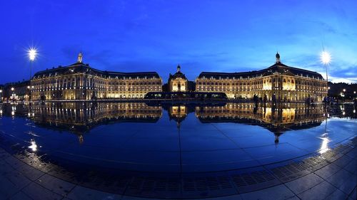 Illuminated castle reflection in water at place de la bourse against sky