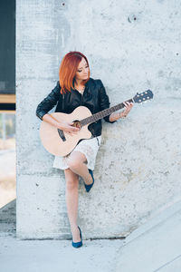 Full length of woman playing guitar against wall