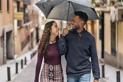 Cheerful couple holding umbrella walking outdoors