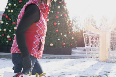 Midsection of woman standing against christmas tree during winter