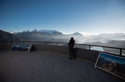 Rear view of man standing on railing against mountain