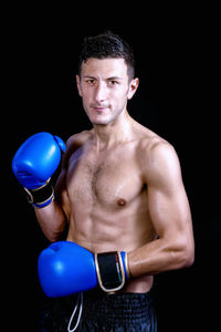 Portrait of shirtless male boxer standing against black background