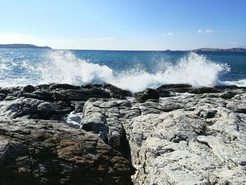 Waves splashing on rocks against clear sky