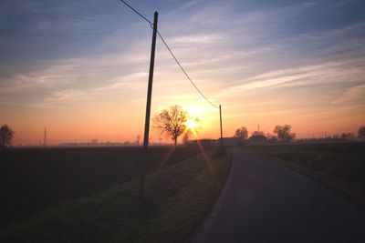 Road amidst silhouette field against sky during sunset