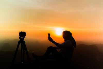 Silhouette woman taking selfie against orange sky