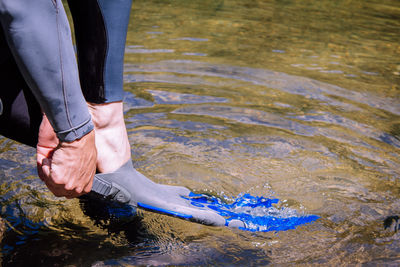 Low section of man wearing diving flippers while standing on lake