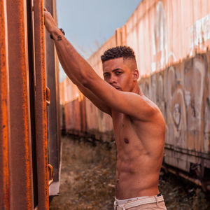 Portrait of shirtless man standing by metal structure