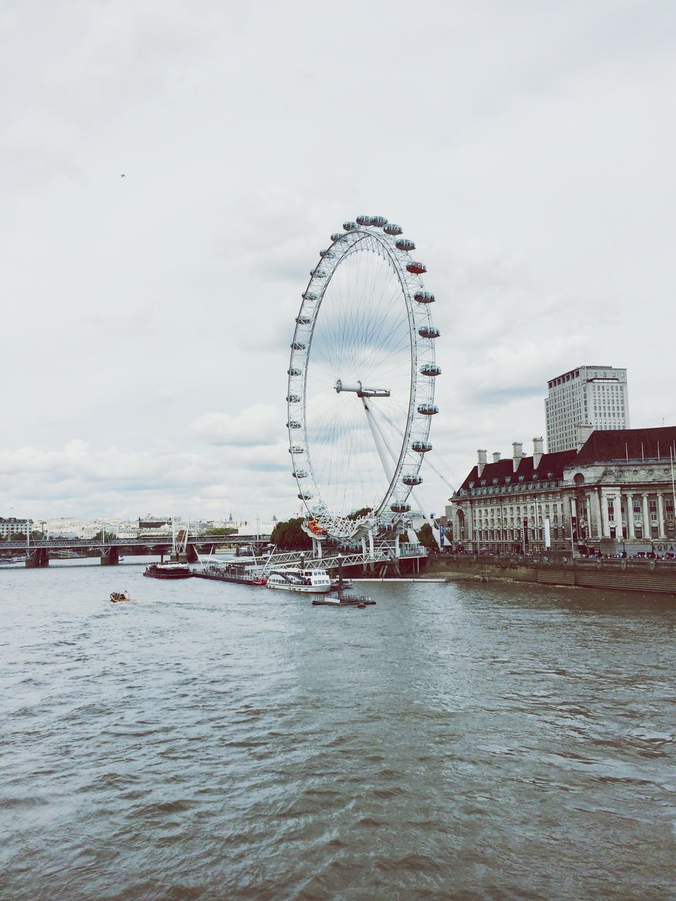 ferris wheel, architecture, built structure, amusement park, amusement park ride, building exterior, sky, arts culture and entertainment, water, waterfront, city, travel destinations, cloud - sky, tourism, travel, river, famous place, tall - high, circle, day