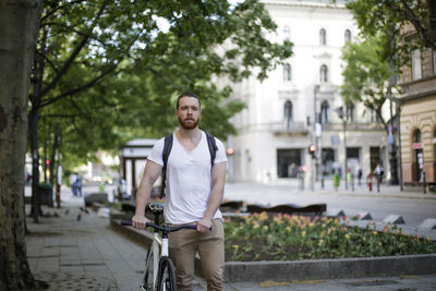 Portrait of man with bicycle standing on street in city