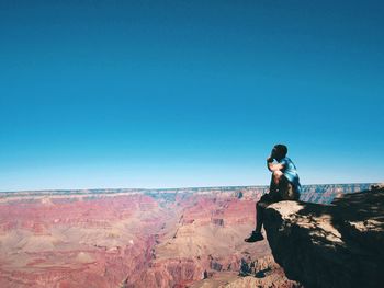 Man sitting on cliff against clear sky