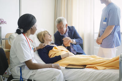 Healthcare workers looking at senior man consoling patient in hospital ward