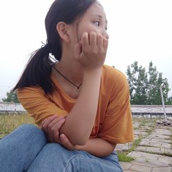 Young woman looking away while sitting against clear sky