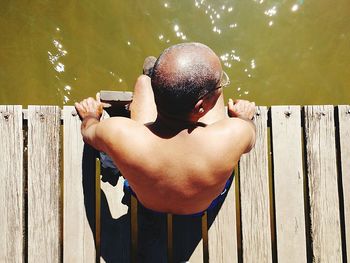 Rear view of shirtless man standing on wooden pier over lake