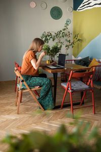 Woman with glass cup of tea works online at home by laptop on table