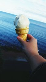 Cropped hand holding ice cream cone against sea
