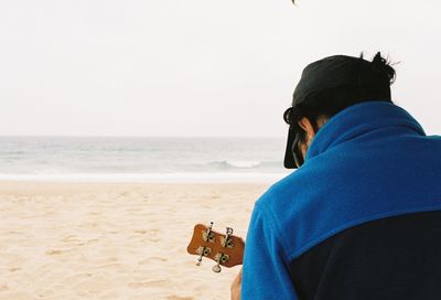 Rear view of man playing guitar on beach