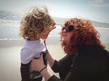 Smiling mother and son at beach against sky