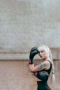 Portrait of woman with boxing gloves standing against wall