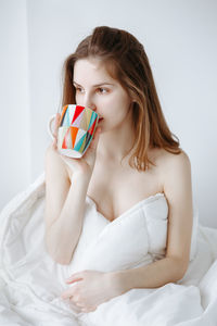 Young woman having drink while sitting on bed