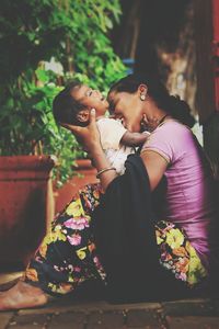 Cheerful mother sitting with daughter against plants